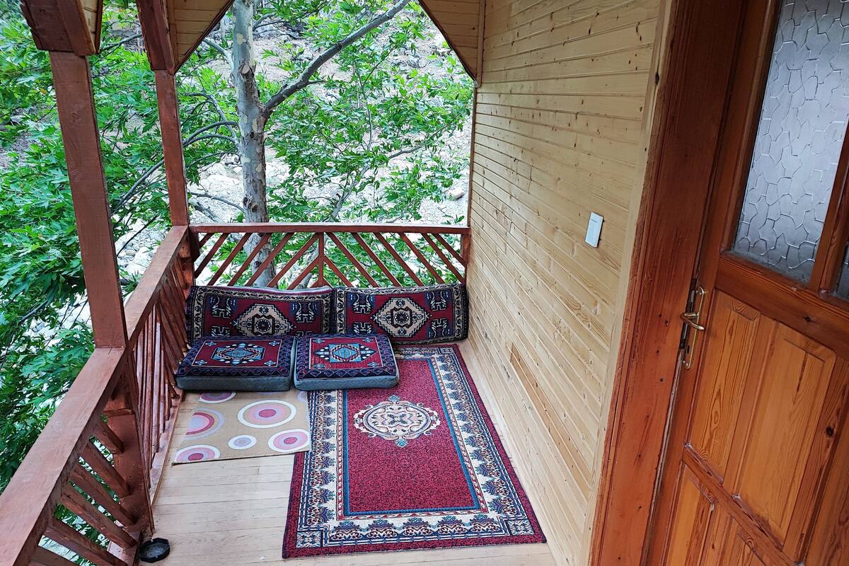 Une terrasse en bois avec un banc et des coussins, une porte et une vue sur la verdure.