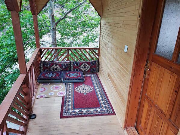 Une terrasse en bois avec un banc et des coussins, une porte et une vue sur la verdure.