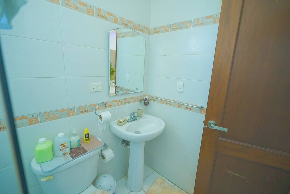 A small bathroom with a toilet, sink, and mirror. There are toiletries on the sink counter.