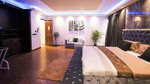 Un dormitorio moderno con una cama grande, un sofá, un ventilador y obras de arte en la pared.