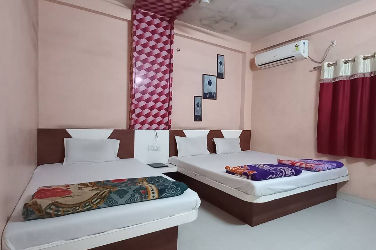 A hotel room with two beds, a patterned curtain, an air conditioning unit, and wall-mounted pictures.