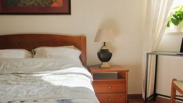 Una cama bien hecha con un edredón a rayas, una mesita de noche con lámpara, una pequeña mesita auxiliar de madera y una silla.