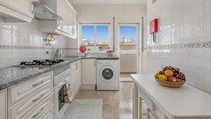 A modern kitchen with white cabinets, a built-in oven, a washing machine, and a fruit bowl on the counter. - Sunny and Spacious Apartment with Balcony! Walk to Beach & Town (Lagos)