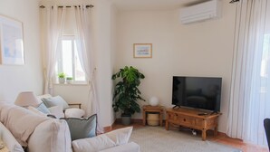 A living room with a sofa, TV, potted plants, and a wooden cabinet. - Sunny and Spacious Apartment with Balcony! Walk to Beach & Town (Lagos)