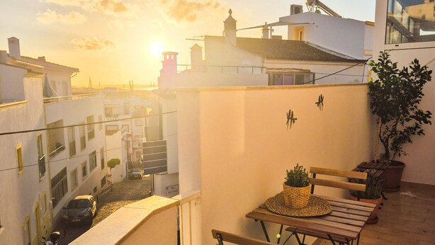 A balcony with a table and chairs, overlooking a cityscape during sunset. - Sunny and Spacious Apartment with Balcony! Walk to Beach & Town (Lagos)