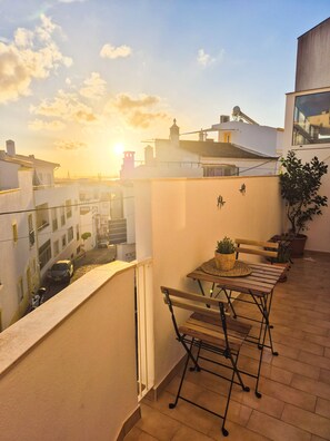 A balcony with a table and chairs, overlooking a cityscape during sunset.