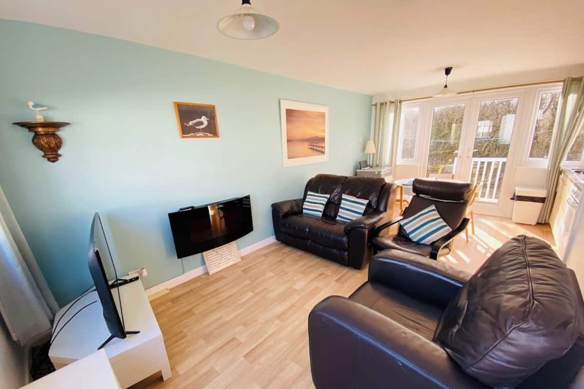 A living room with a TV, two leather sofas, a white side table, and a wooden floor.