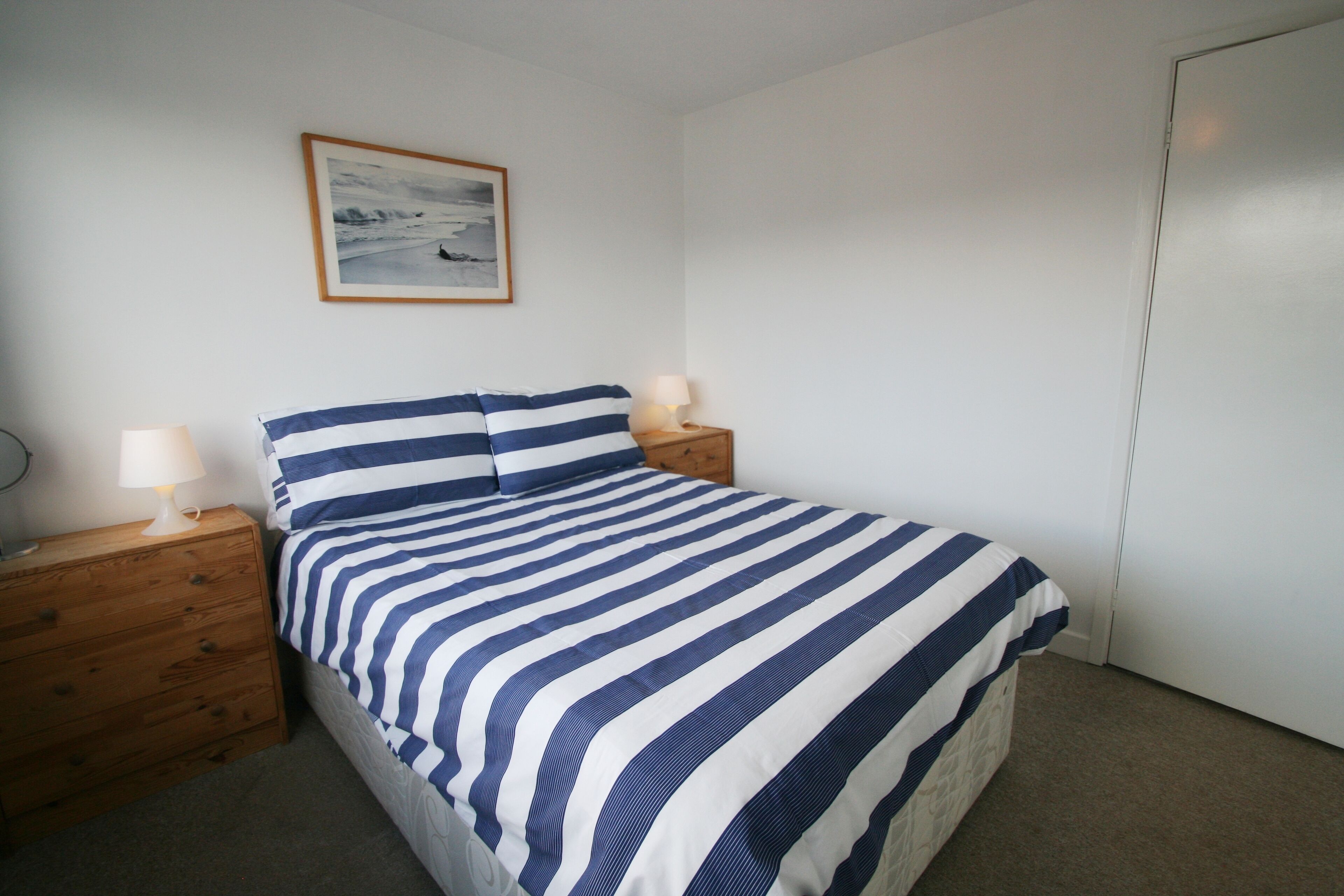 Una camera da letto con un letto, due comodini, una lampada su ciascuno e un quadro appeso al muro.