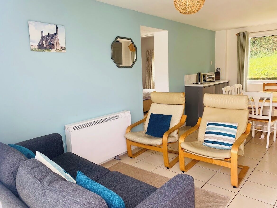 Un salon comprenant un canapé, deux fauteuils, une petite table et une vue sur le jardin par une fenêtre.