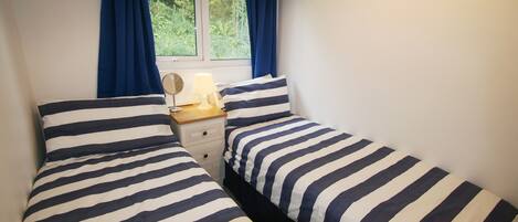 A bedroom with two beds, a bedside table with a lamp, and a window with curtains.