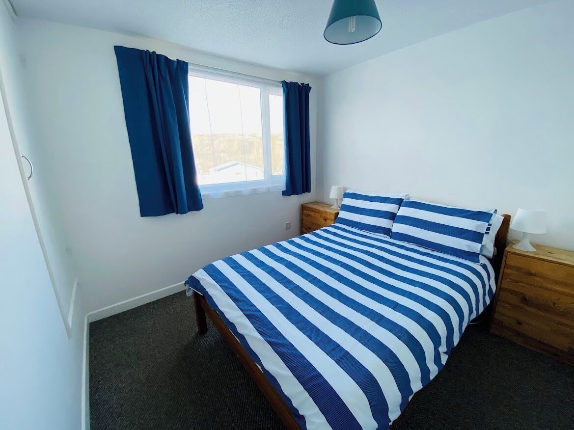 A bedroom with a bed, a nightstand, a lamp, and a window with curtains.