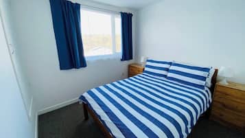 A bedroom with a bed, a nightstand, a lamp, and a window with curtains.