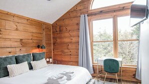 A wooden-paneled bedroom with a bed, a desk, and a view through a window.