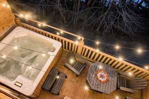 A hot tub, wooden deck, Adirondack chairs, and string lights.