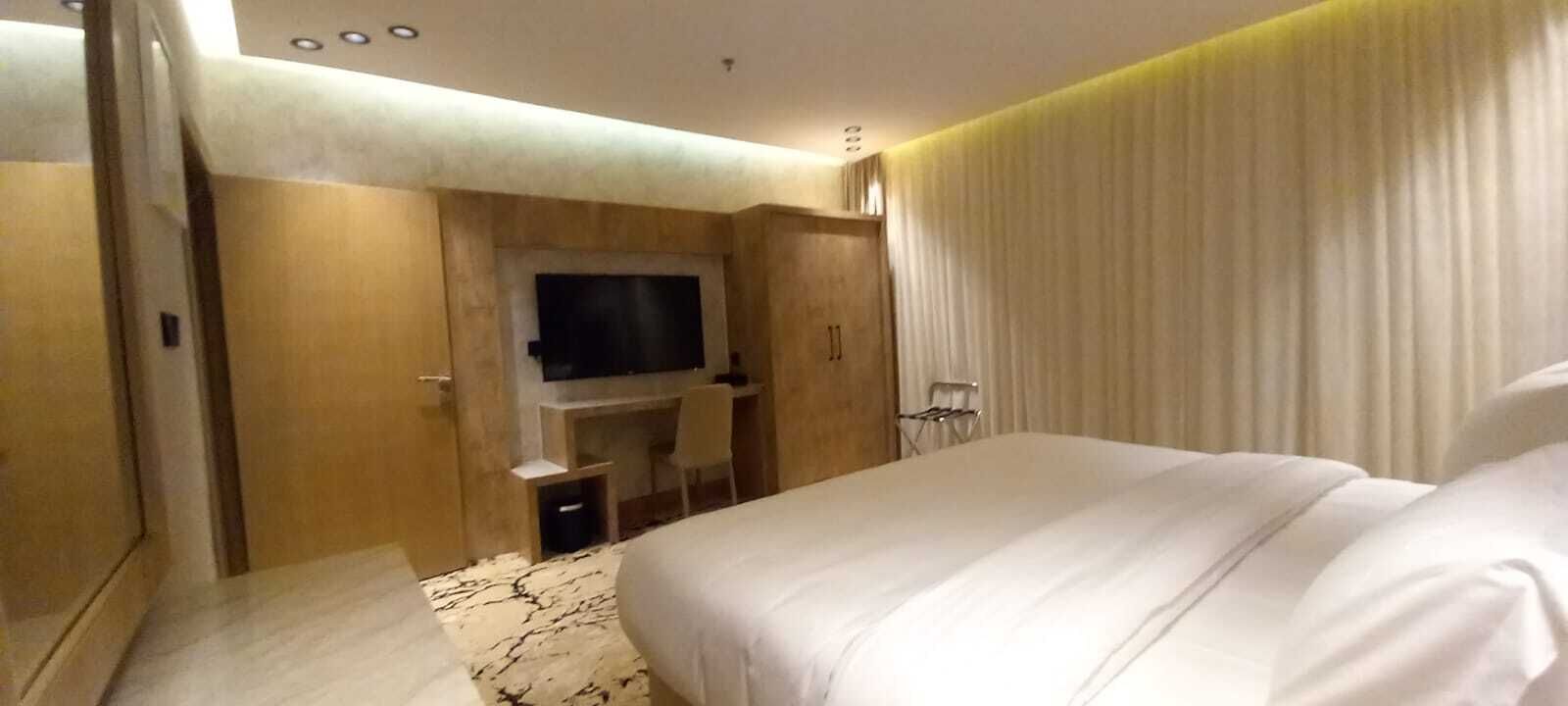 Una habitación de hotel moderna con una cama grande, un televisor de pantalla plana montado en la pared, un escritorio con una silla y un ventanal con cortinas.