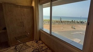 Une chambre dotée d’une grande fenêtre donnant sur une plage et un parking.