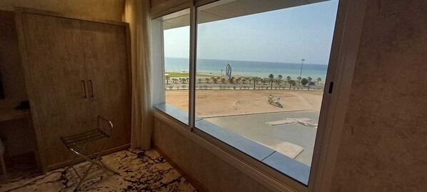 Une chambre dotée d’une grande fenêtre donnant sur une plage et un parking.