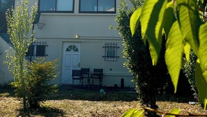 Une maison à deux étages, avec un toit en tuiles, une porte d’entrée et un petit jardin agrémenté d’un arbre et d’un panier de basket.