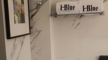 Un baño con un inodoro, un perchero con dos toallas, un cuadro enmarcado en la pared y un revestimiento de pared con diseño de mármol.