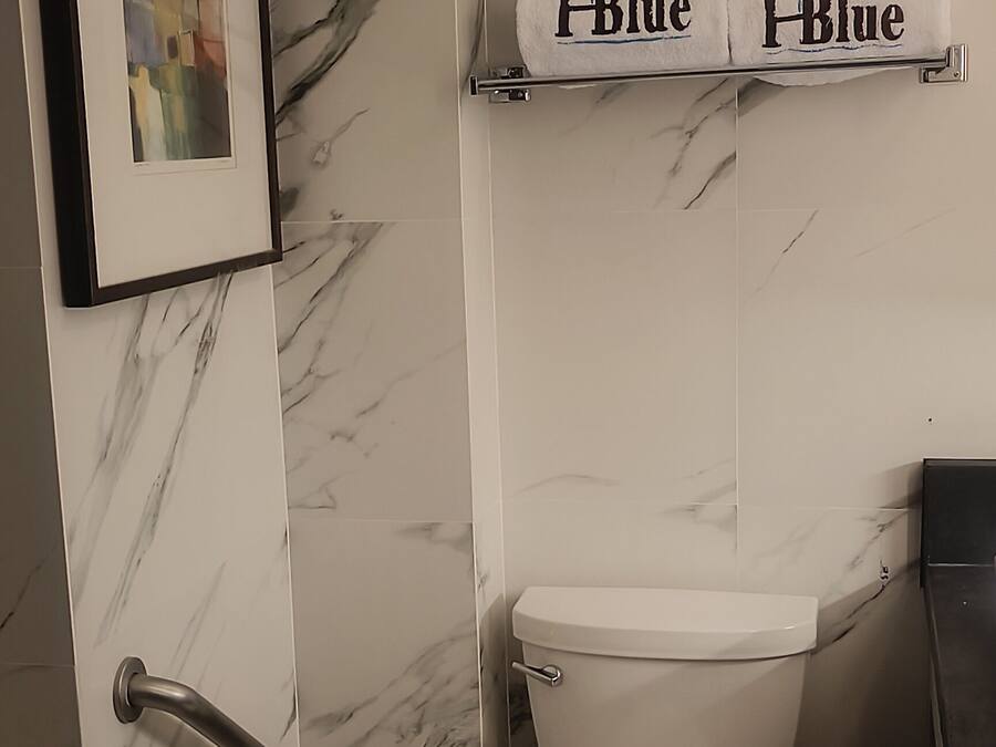 Un baño con un inodoro, un perchero con dos toallas, un cuadro enmarcado en la pared y un revestimiento de pared con diseño de mármol.