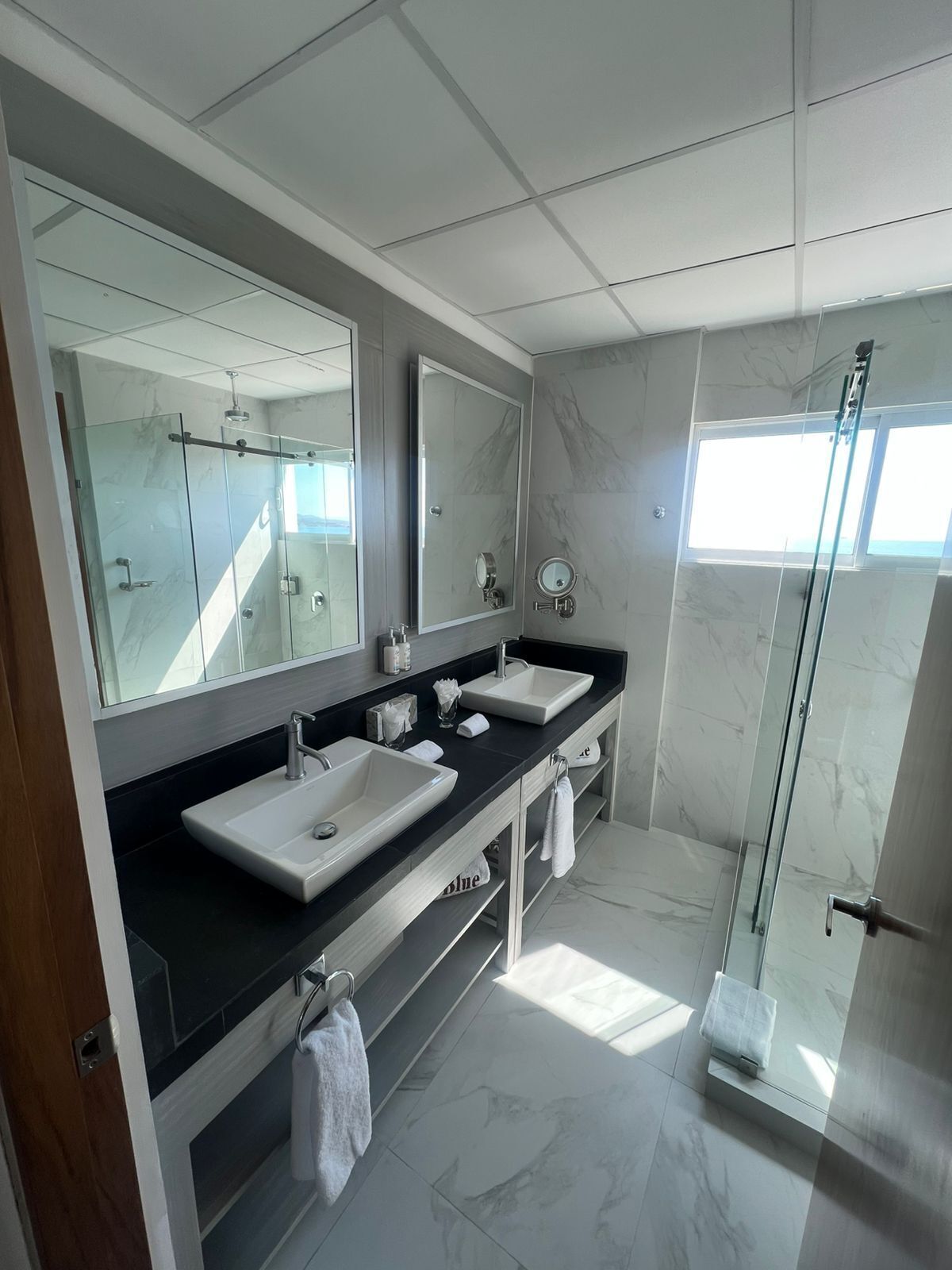 A modern bathroom with two sinks, a large mirror, and a glass shower enclosure.