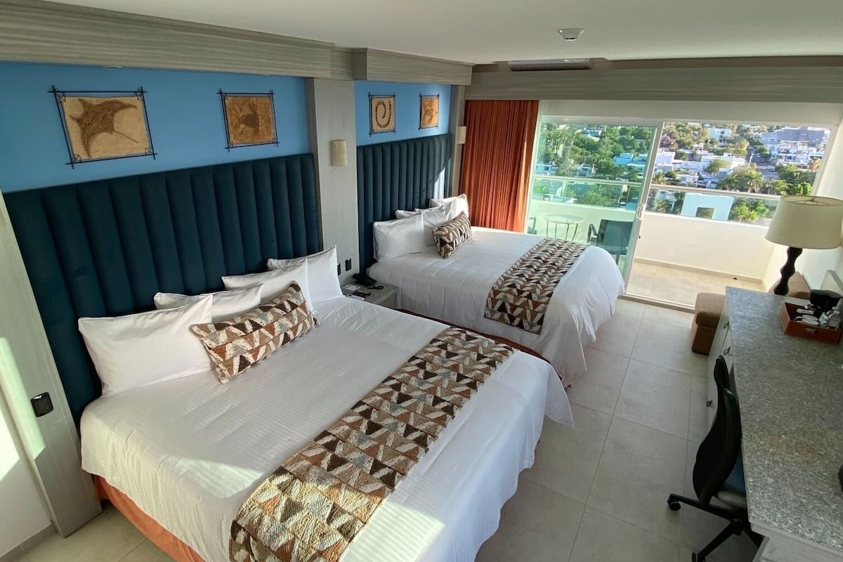 Une chambre d’hôtel avec deux lits, un balcon offrant une vue et un bureau avec une lampe.