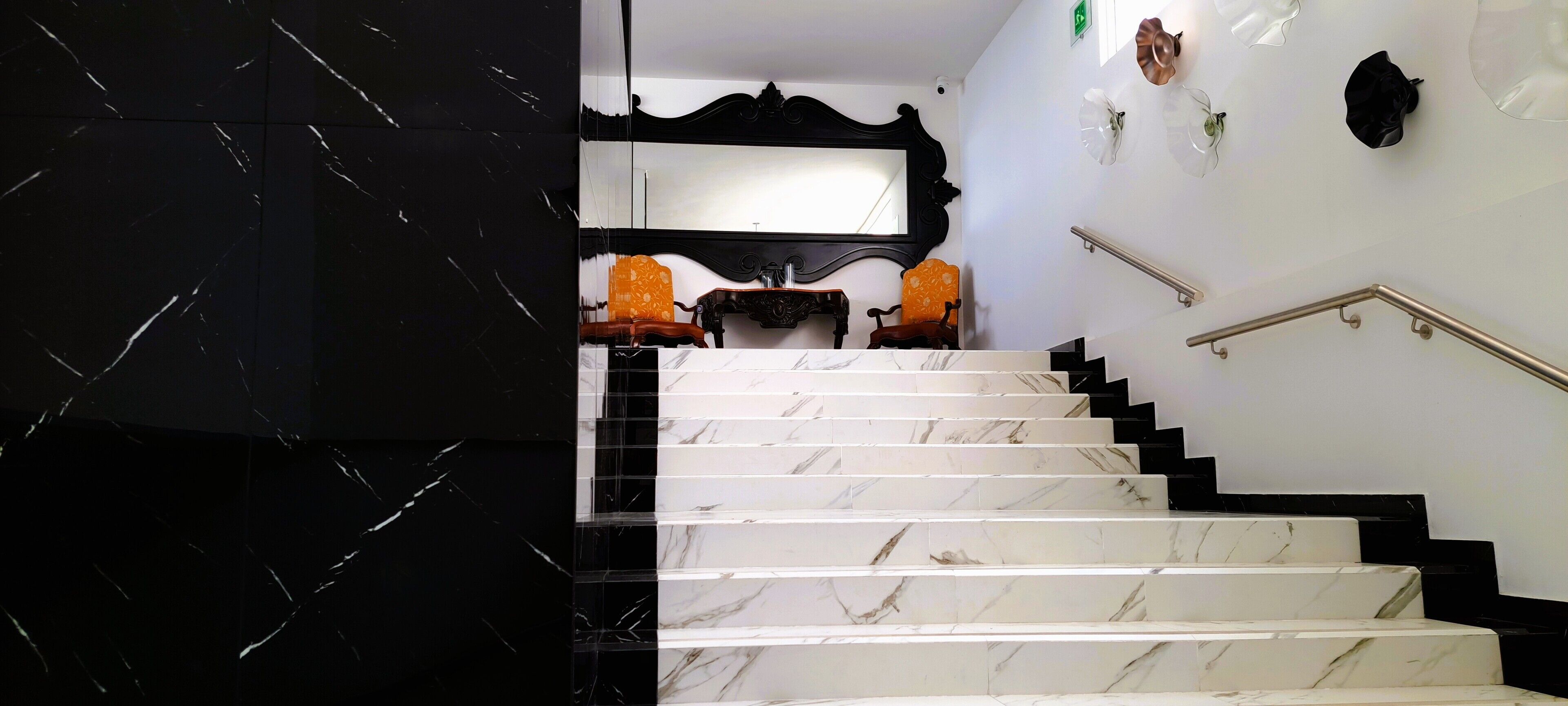 A marble staircase with black and white marble steps, a black wall with a mirror, and two orange chairs.