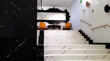 A marble staircase with black and white marble steps, a black wall with a mirror, and two orange chairs.