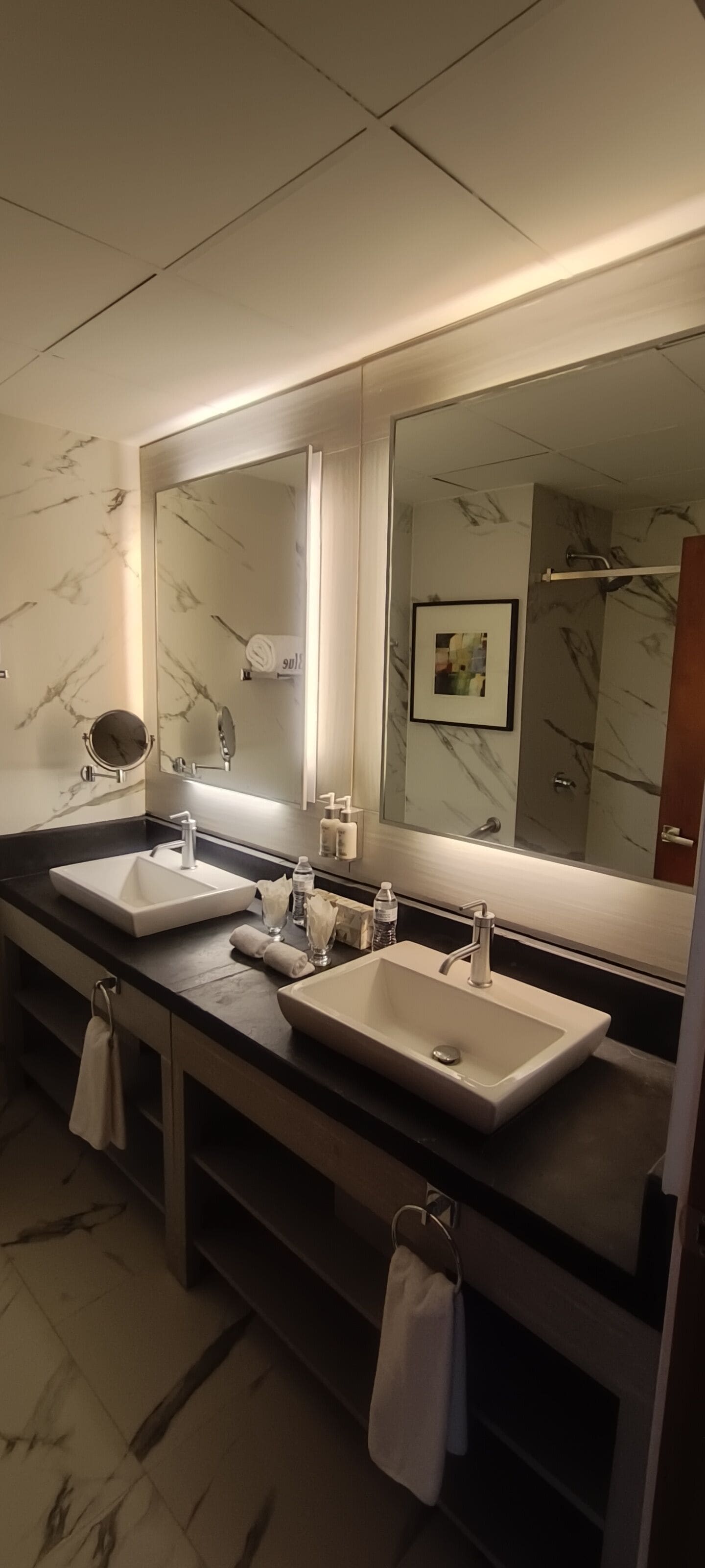 Un baño moderno con dos lavamanos, un espejo grande y paredes con diseño de mármol.