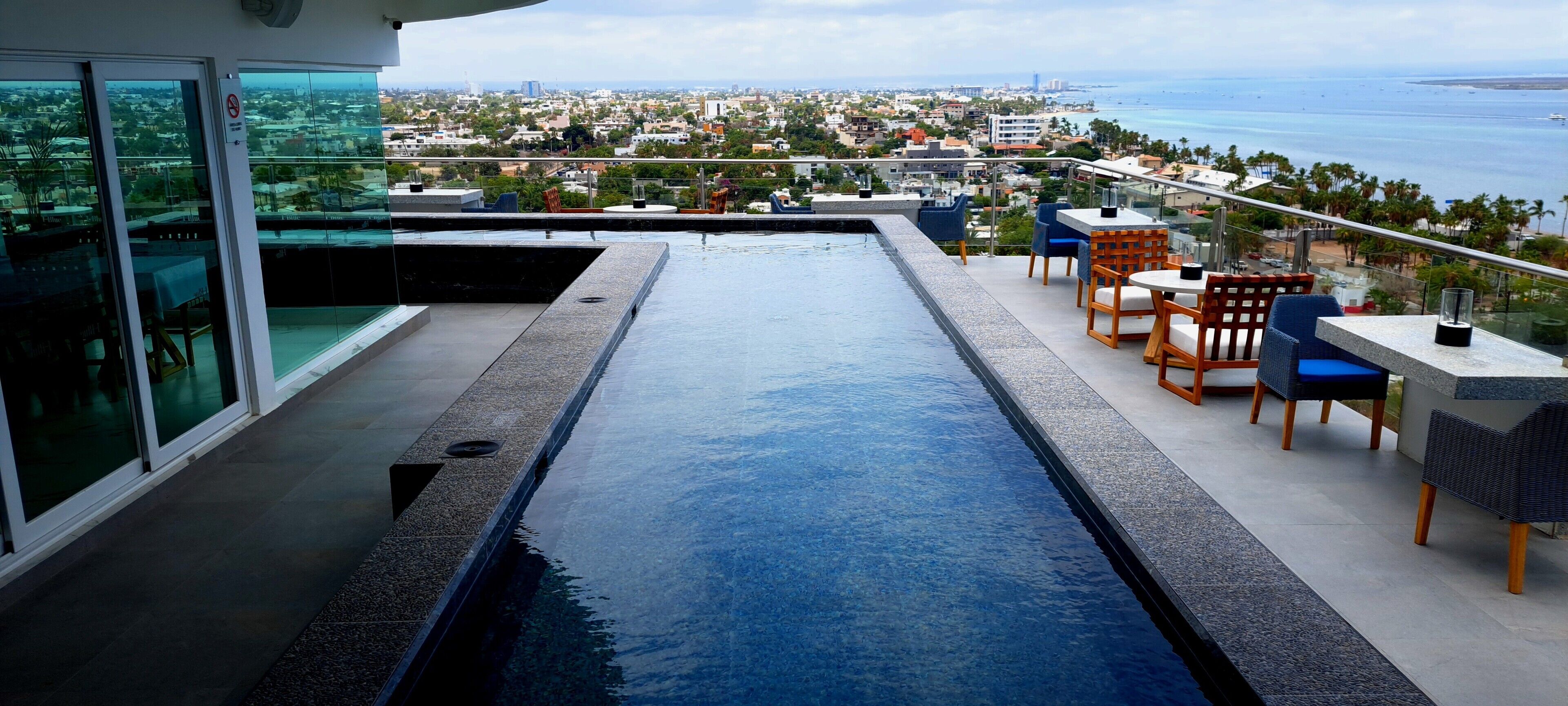 Una piscina en la azotea con vista a la ciudad, mobiliario exterior y una zona con cerramiento de cristal.