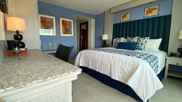 Una habitación de hotel con una cama, un escritorio y una silla. Hay dos lámparas sobre el escritorio y una puerta que da a otra habitación.