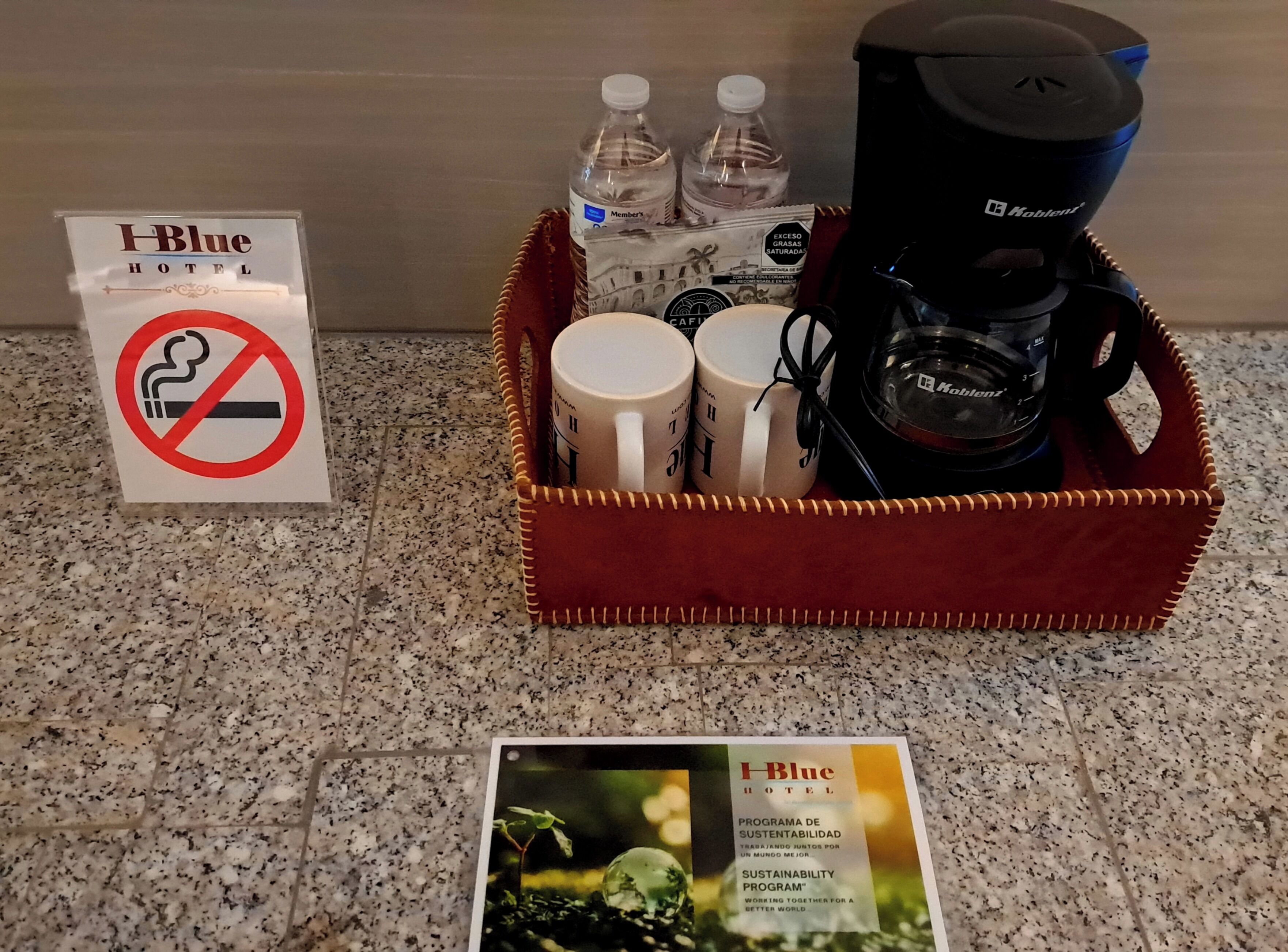 A hotel room with a coffee maker, water bottles, and mugs on a countertop. A no-smoking sign is visible.