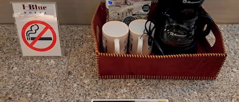 A hotel room with a coffee maker, water bottles, and mugs on a countertop. A no-smoking sign is visible.