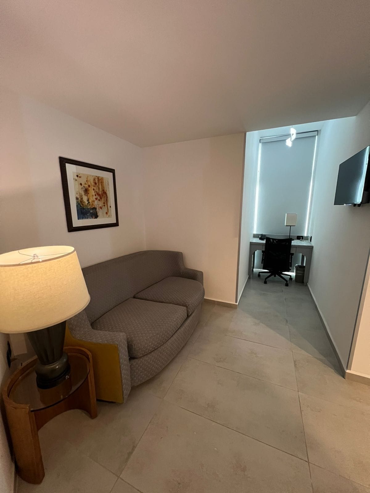 A modern living room with a sofa, a lamp, a framed picture, and a TV mounted on the wall.