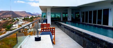 A modern hotel balcony with a pool, overlooking a mountainous landscape.
