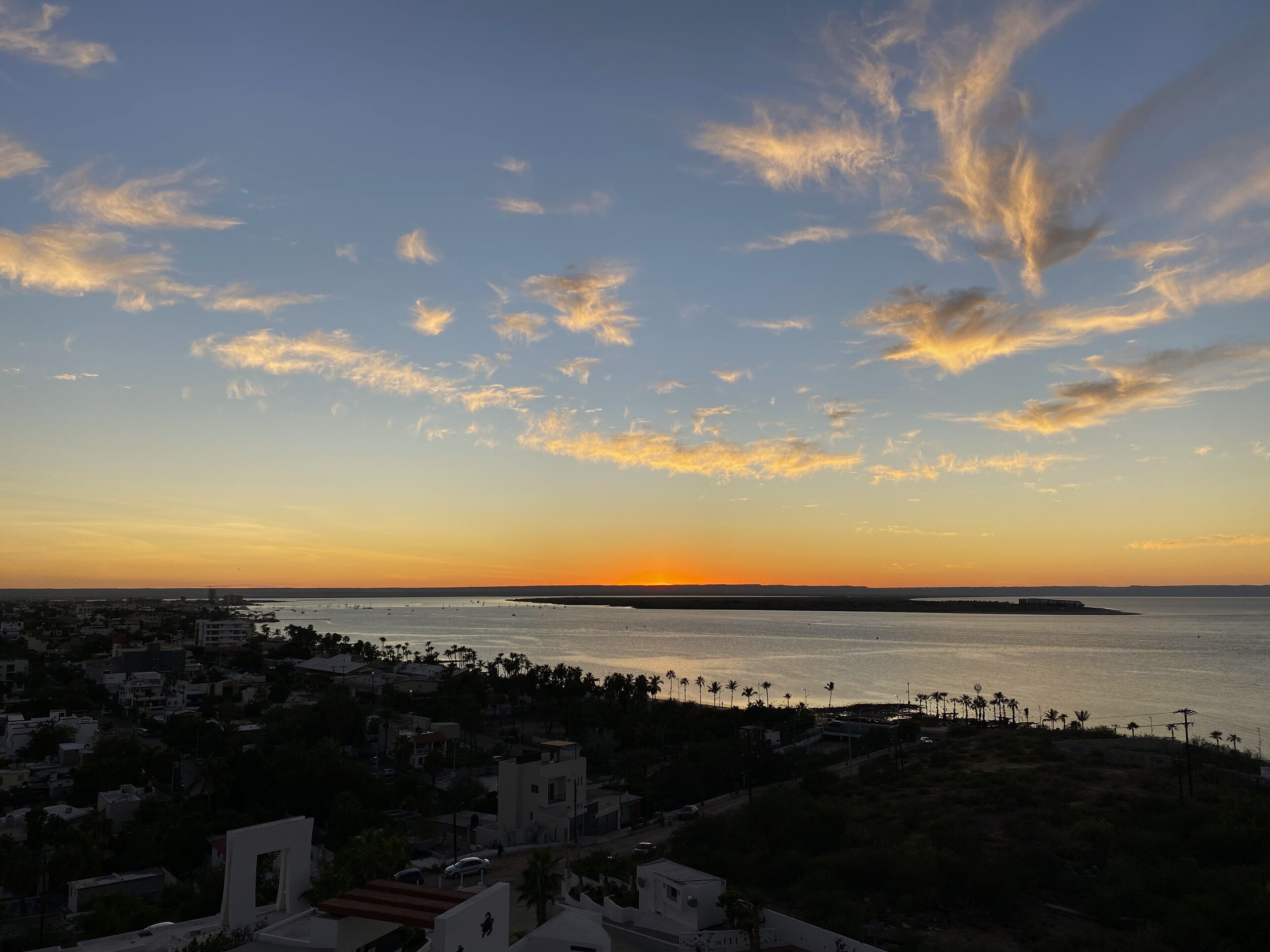 Un paisaje urbano costero al atardecer con cielo despejado, mar tranquilo y edificios residenciales.