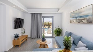 A modern living room with a sofa, a coffee table, a TV, and a view of an outdoor pool area. - calmare collection hotel (Naxos)