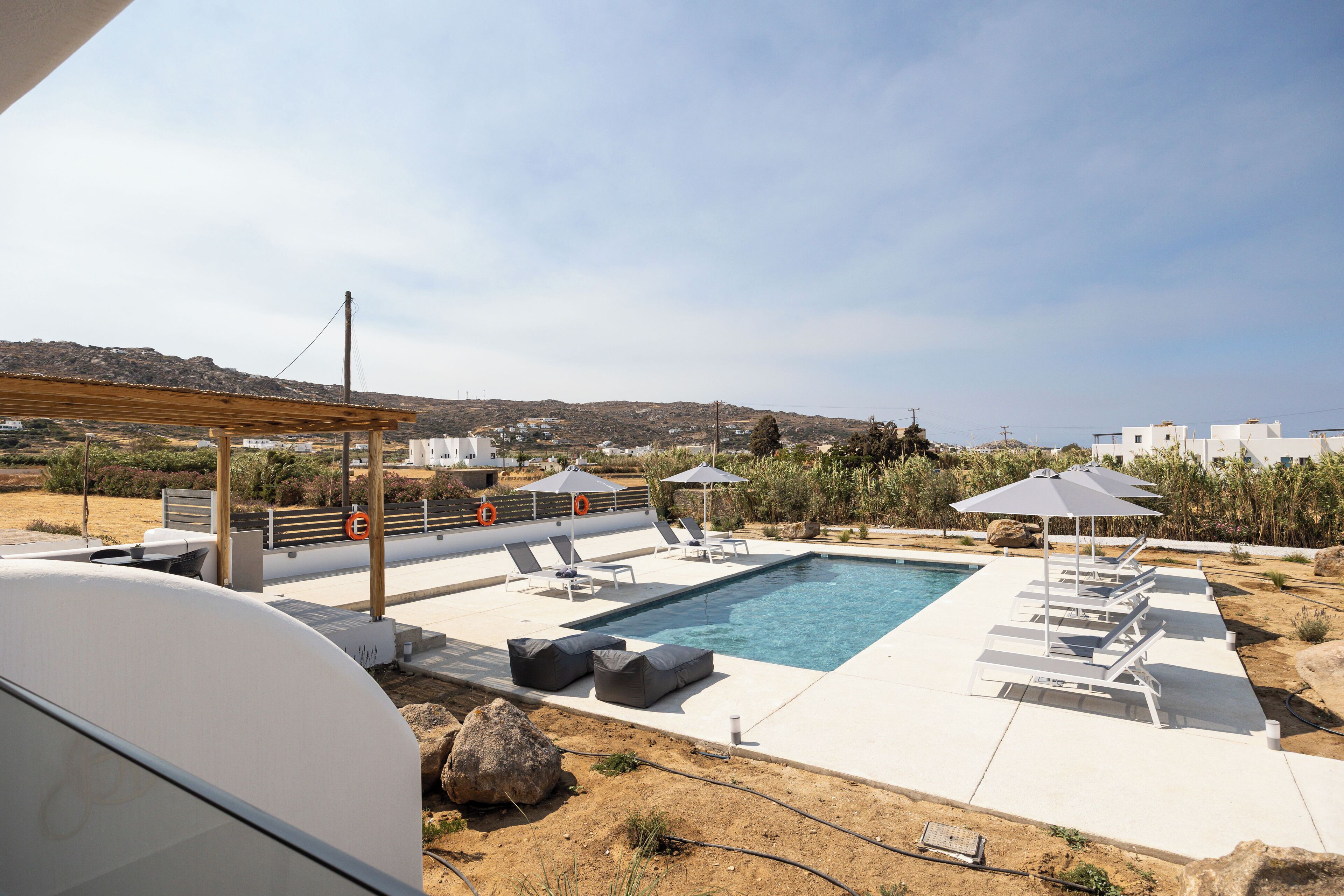 A pool area with lounge chairs and umbrellas, surrounded by a white pool deck and a view of the landscape.