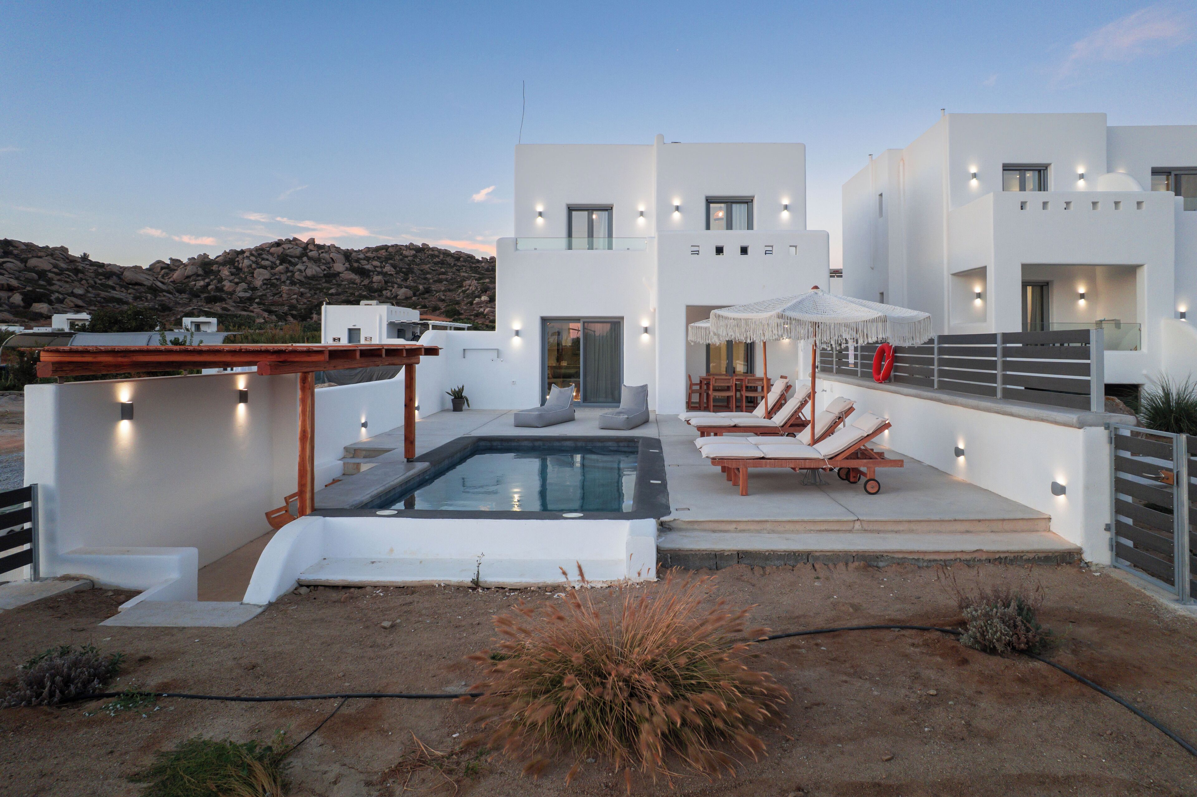 Una villa moderna con piscina, mobiliario de exterior y vistas del paisaje rocoso.