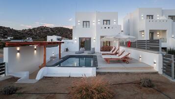 Una villa moderna con piscina, mobiliario de exterior y vistas del paisaje rocoso.