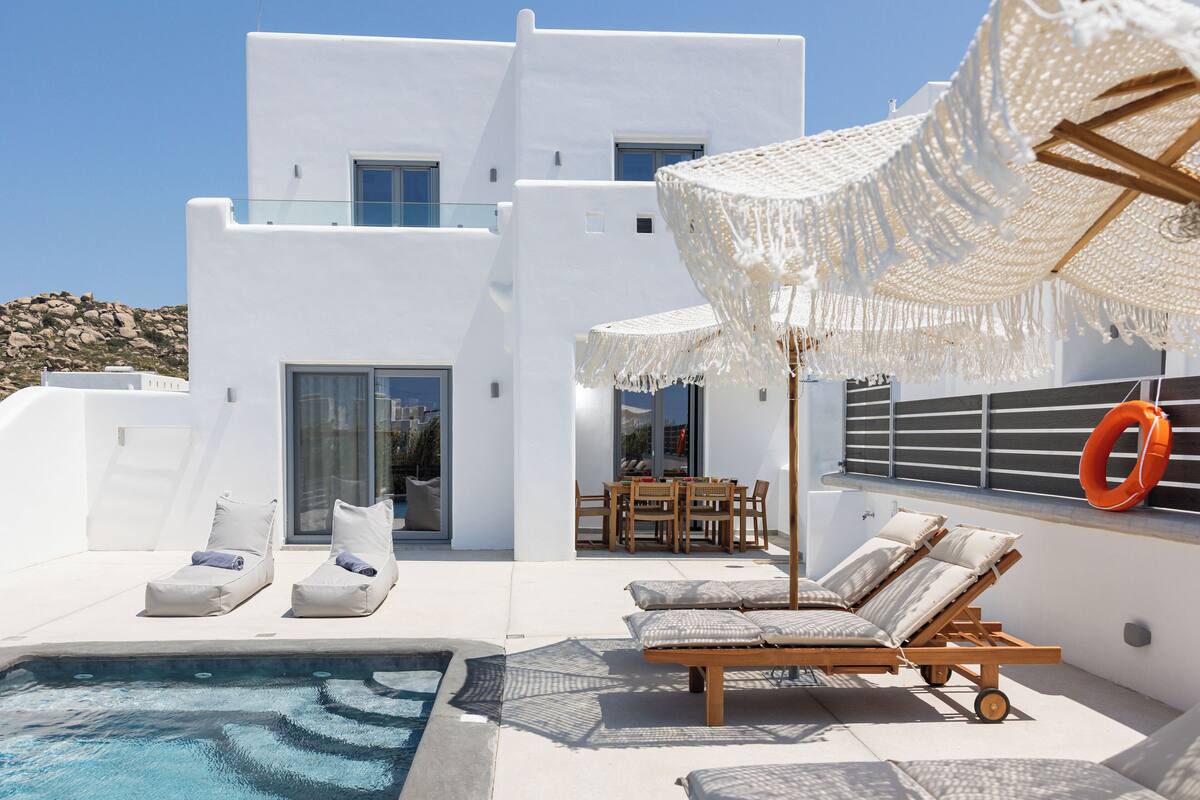 Una villa blanca moderna con piscina, sillones de descanso y zona de comedor.