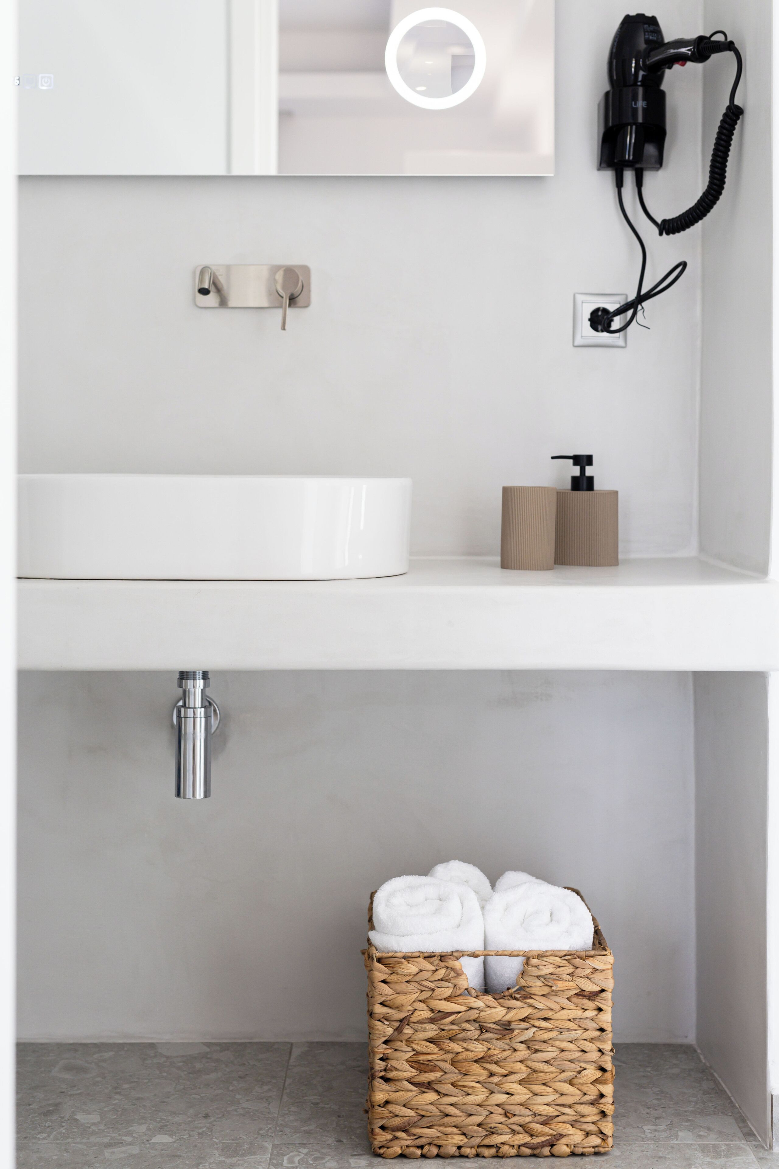 A bathroom with a white sink, a hairdryer, a towel dispenser, and a woven basket with towels.