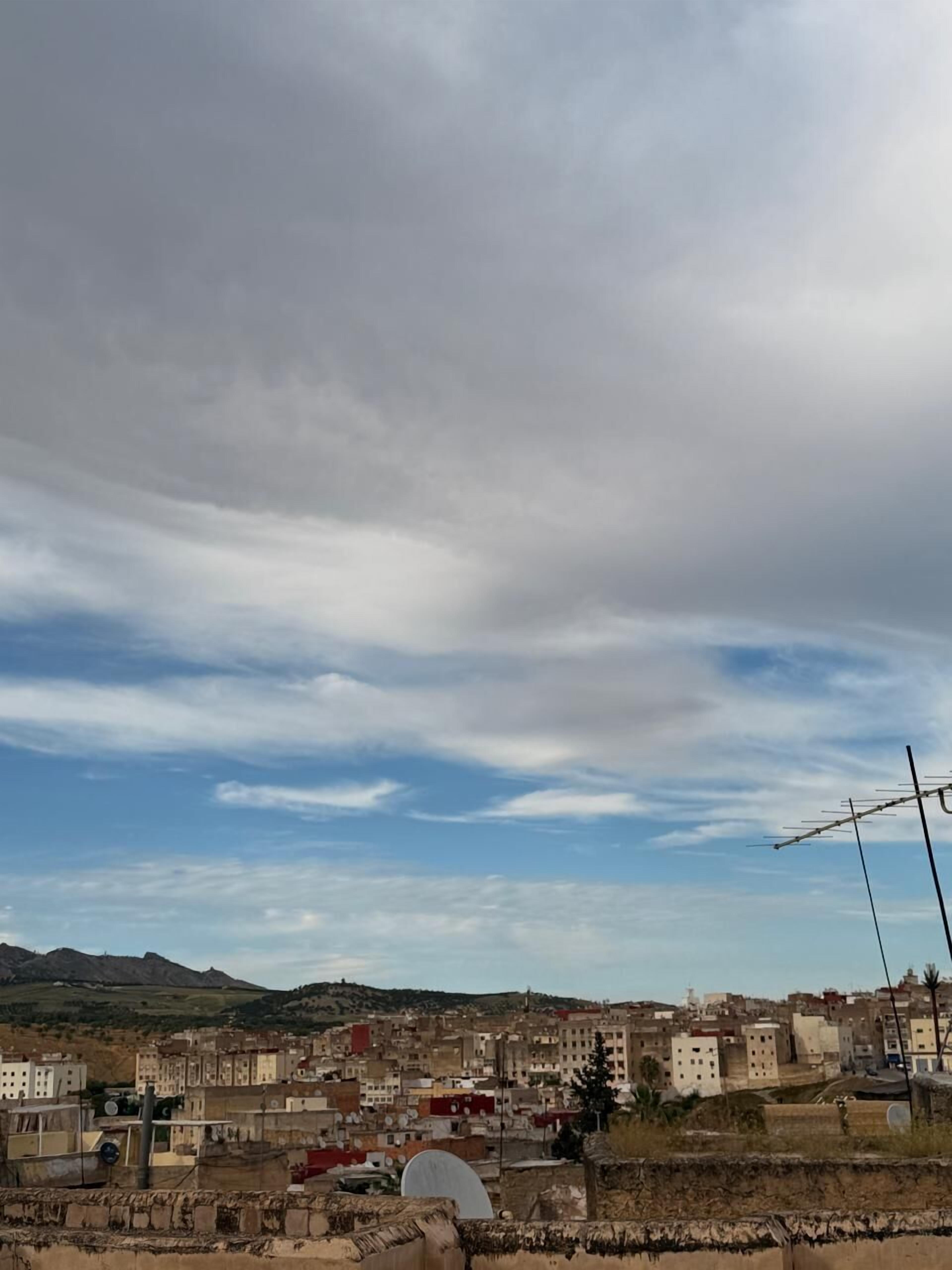 Panorama urbano con edifici, un'antenna parabolica e montagne sullo sfondo.