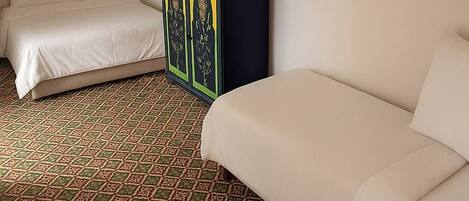 A hotel room with a patterned carpet, a bed, a sofa, and a cabinet with decorative panels.