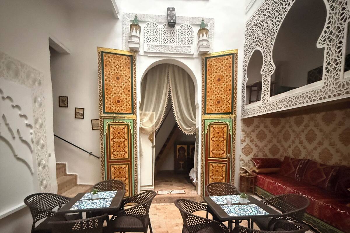 Un interior con un arco central, una zona de estar con mesas y sillas, y un sofá estampado.