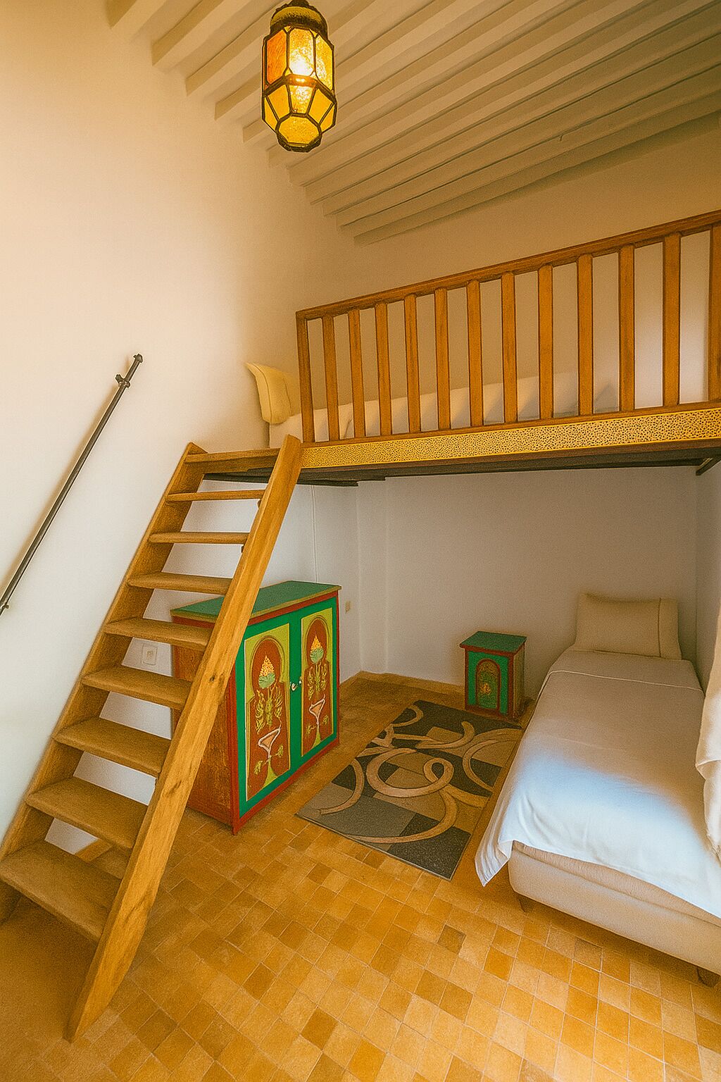A bedroom with a wooden staircase, a bed, a small cabinet, and a decorative rug.