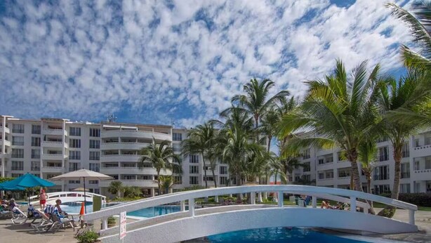 Ein Hotelpoolbereich mit einer weißen Brücke, Palmen und blauem Himmel.