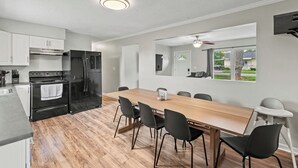 Eine moderne Küche mit Essbereich, ausgestattet mit einem großen Holztisch, schwarzen Stühlen und einem eingebauten Backofen.