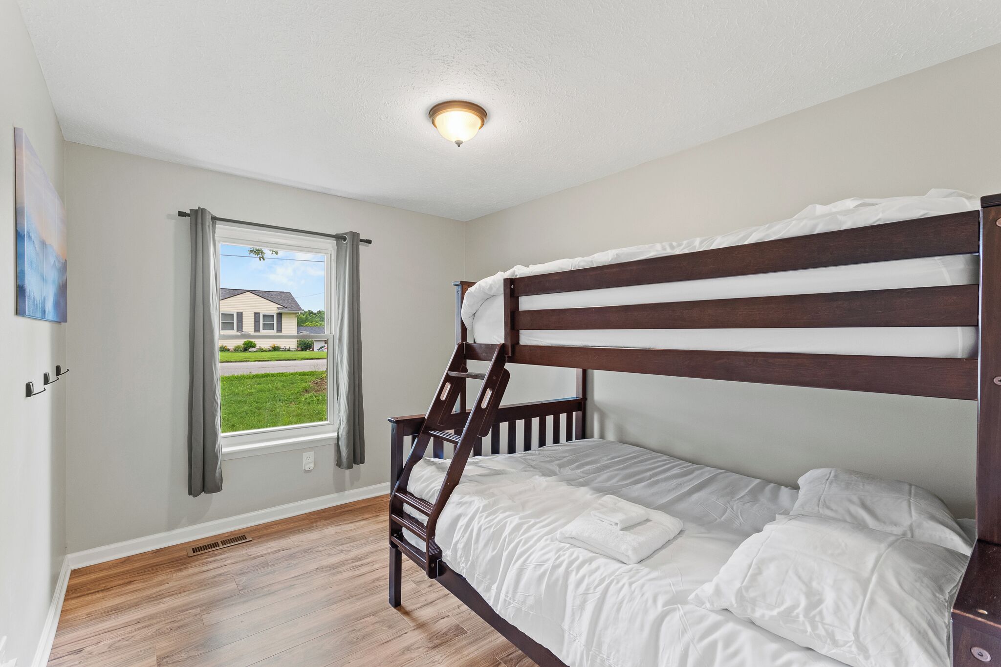 A bunk bed room with a window, a ceiling light, and a view of a house outside.