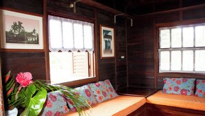Une cabane en bois avec un lit, une fenêtre ornée de rideaux en dentelle et un mur décoré de tableaux encadrés.